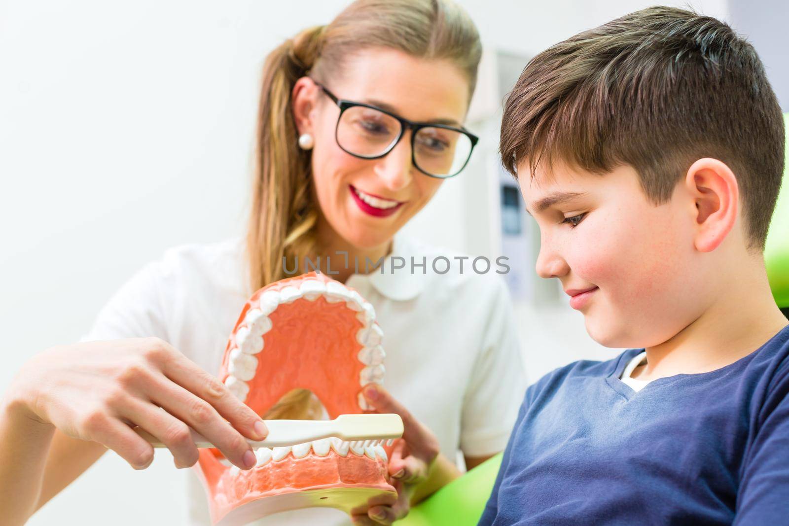 Dentist explaining boy cleaning tooth by Kzenon