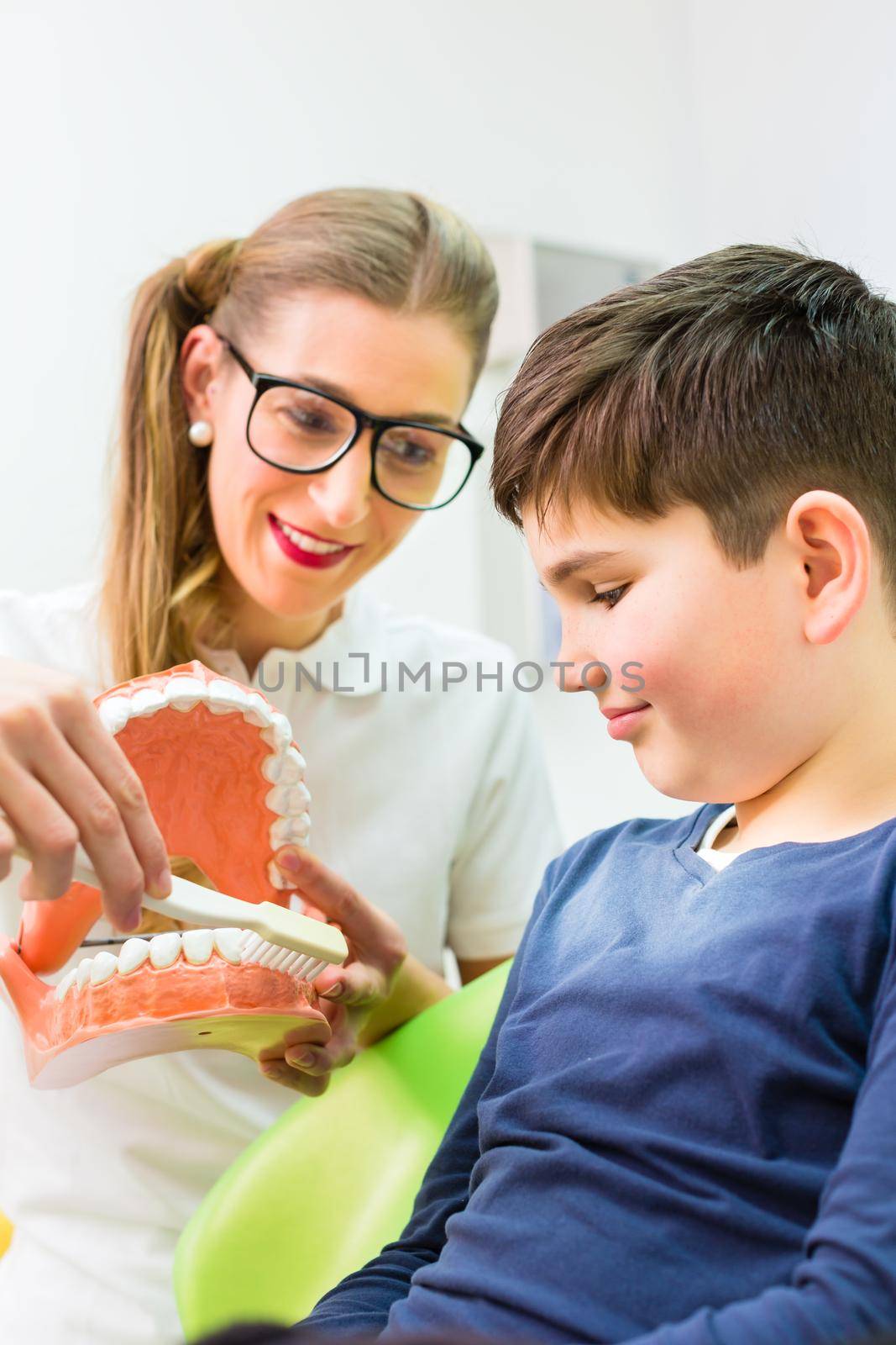 Female dentist explaining boy cleaning tooth with toothbrush on model