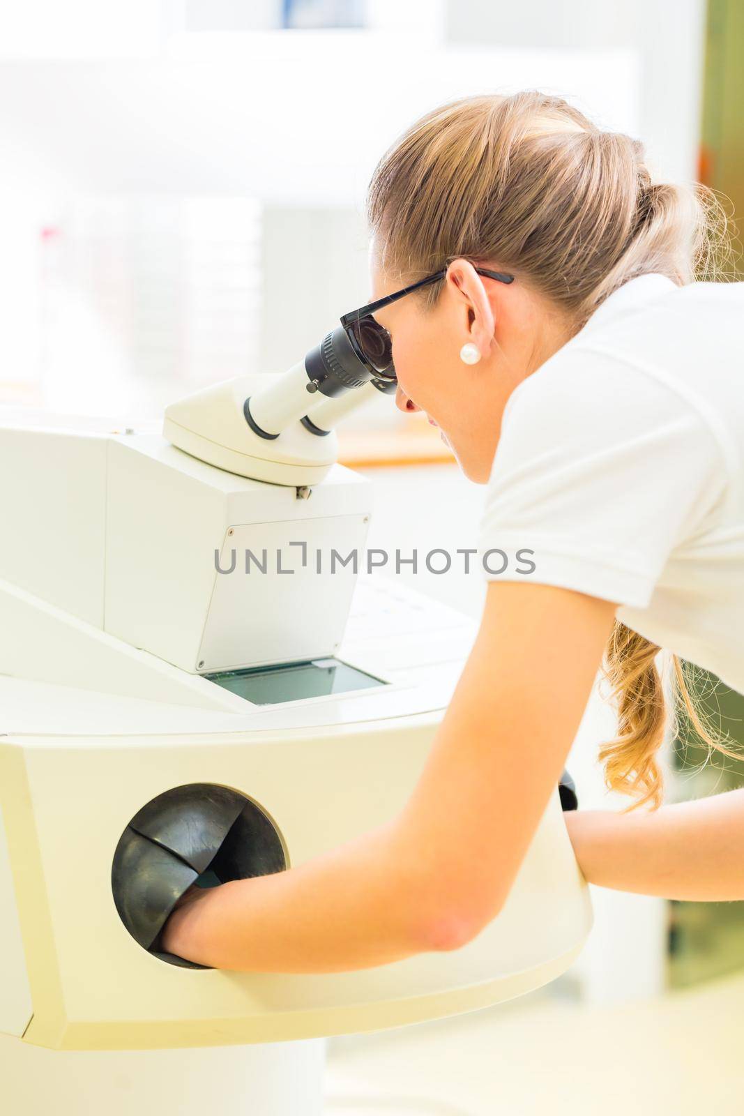 Female dental technician or orthodontist controlling denture with microscope and grinder