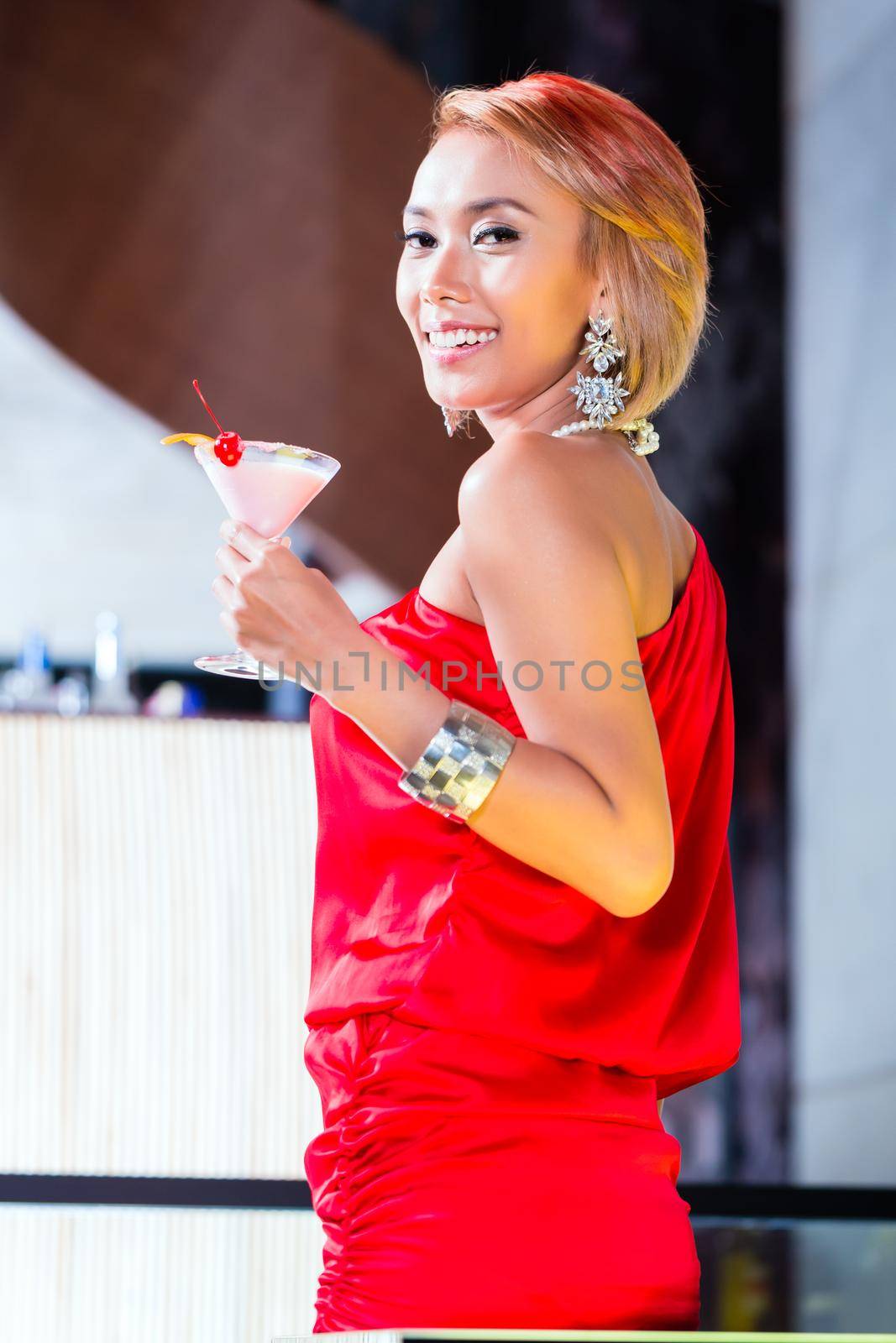 Asian woman drinking cocktails in fancy bar or club by Kzenon