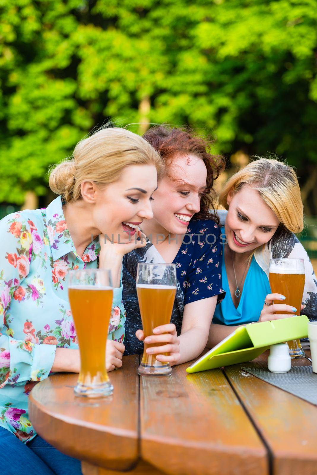 Woman showing friends touch pad in beer garden by Kzenon