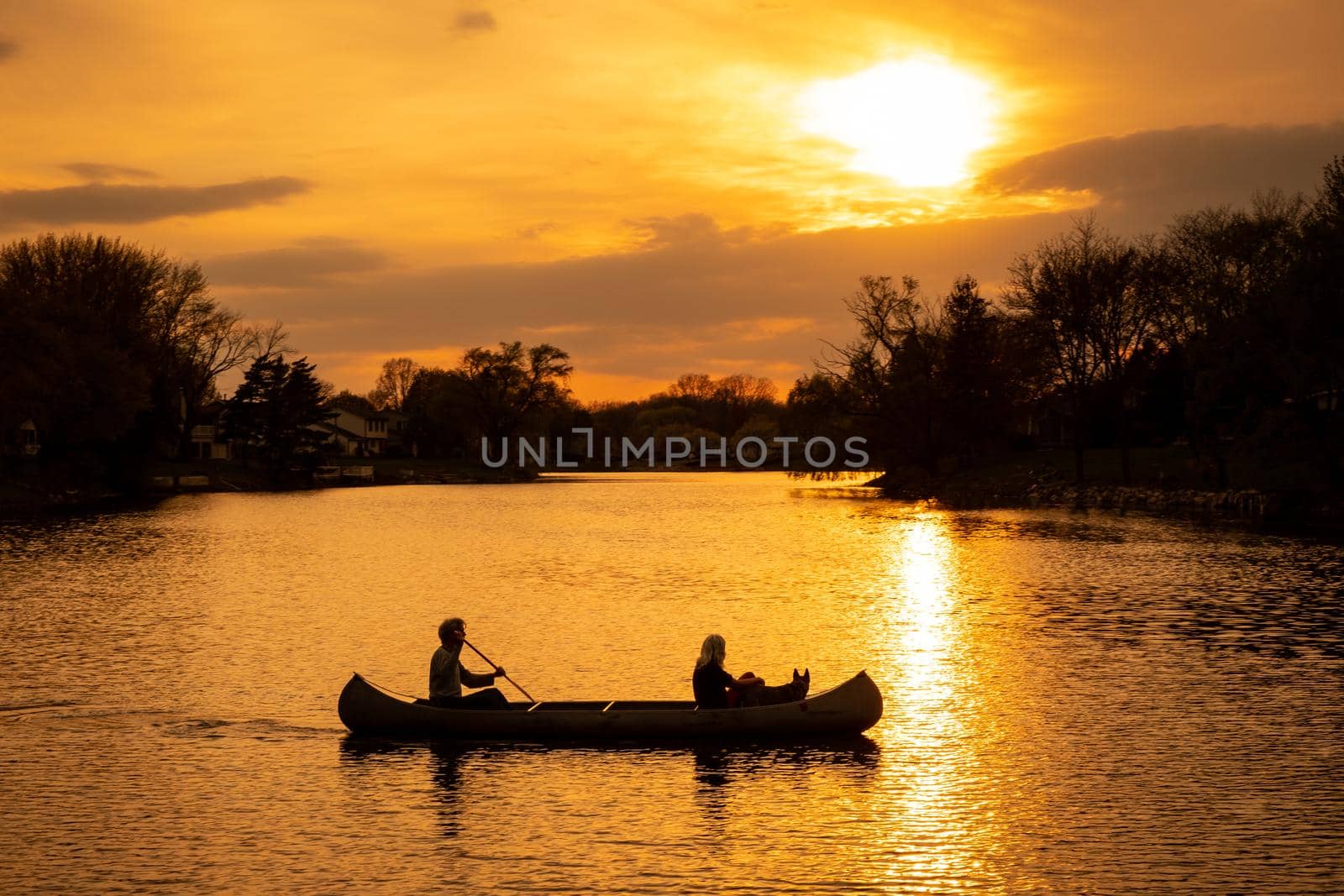 Silhouette of couple with dog kayaking in a lake at sunset, romantic scene