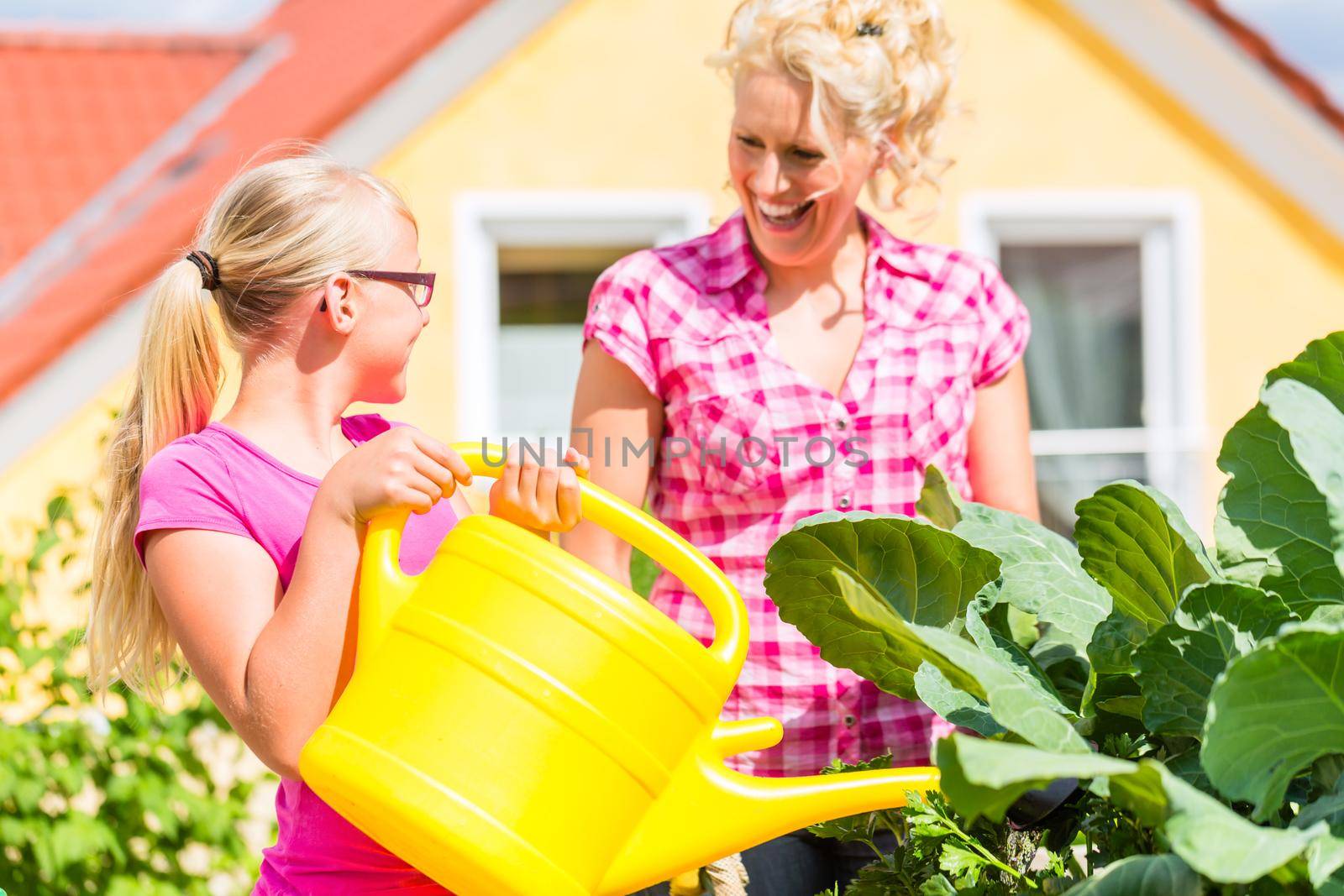 Mother and daughter working in garden watering plants with can in front of their house