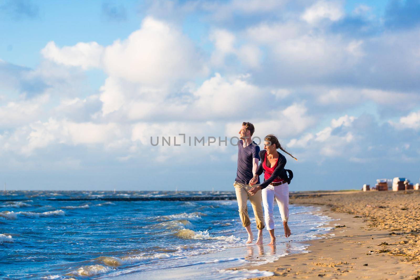 Couple running through sand and waves at beach by Kzenon