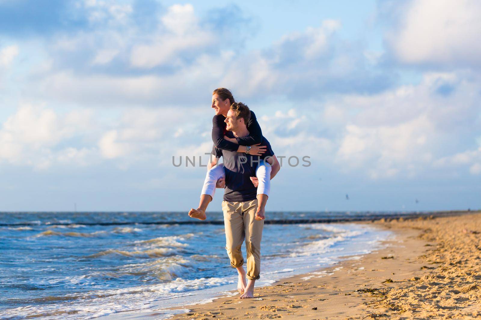 man carrying woman piggyback at beach by Kzenon