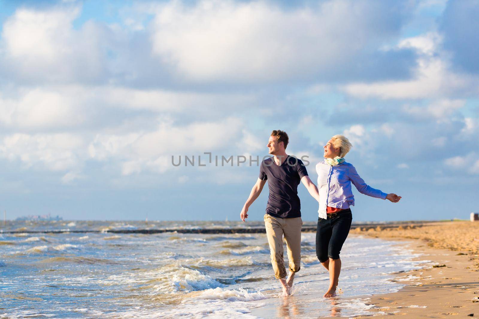 Couple running through sand and waves at beach by Kzenon