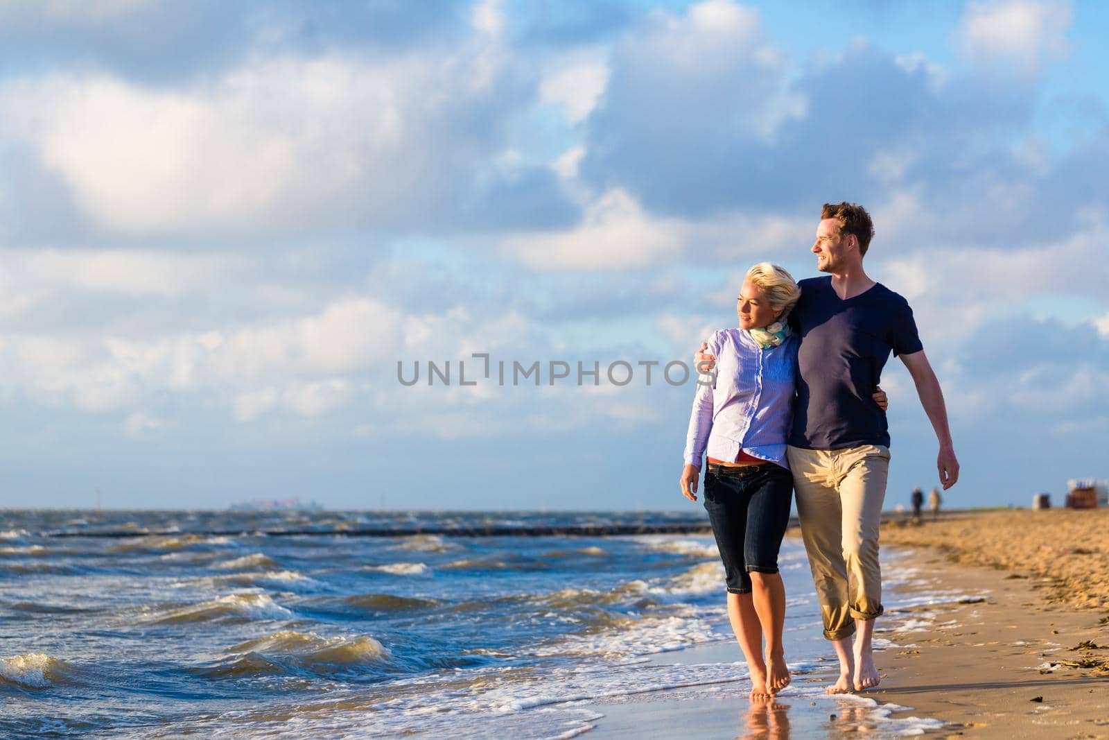 Couple take a romantic walk through sand and waves at German north sea beach