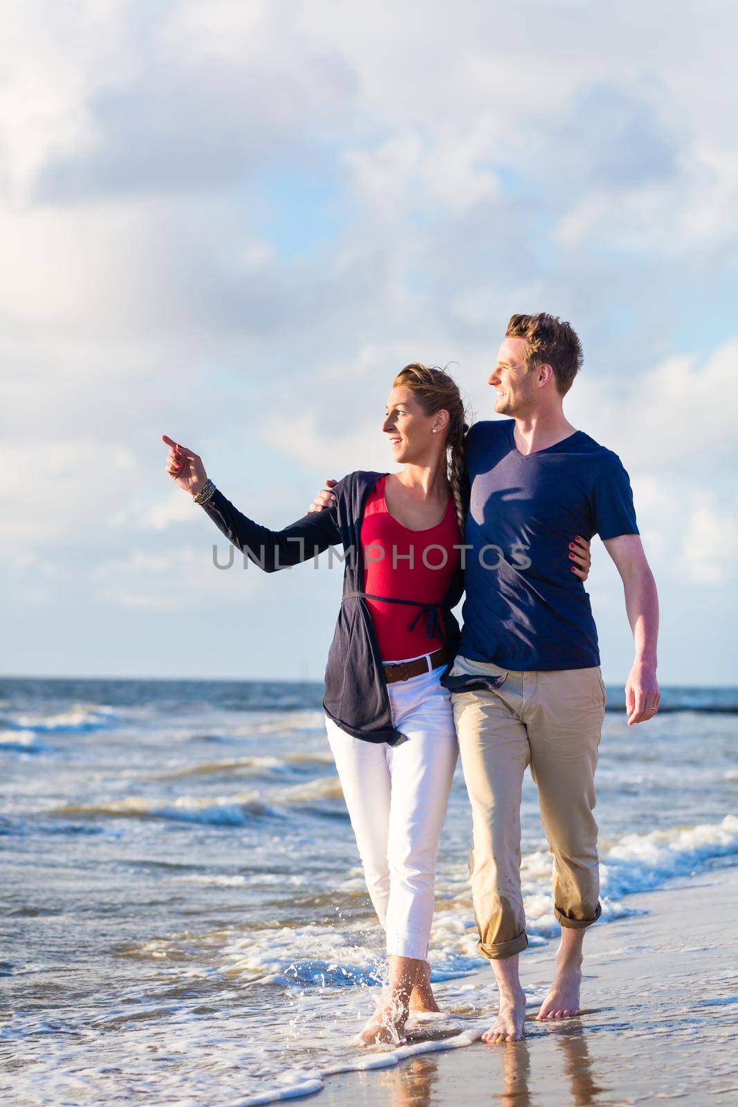 Couple take a romantic walk through sand and waves at German north sea beach