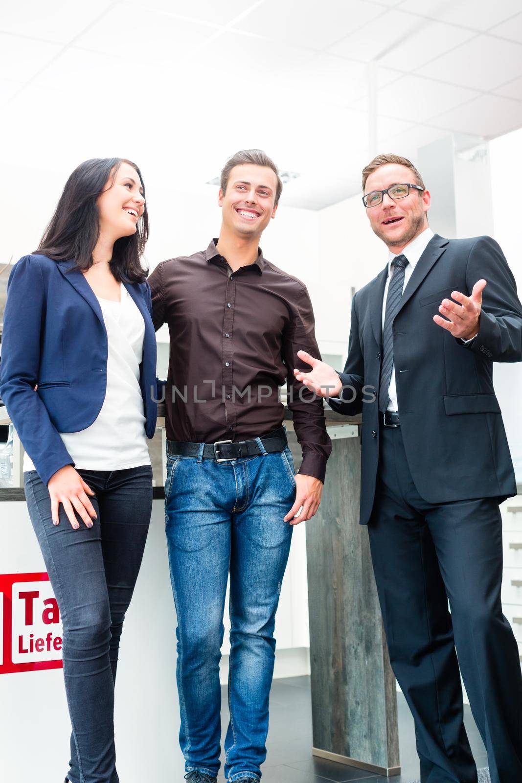 Man and woman consulting salesman for domestic kitchen in studio or furniture store