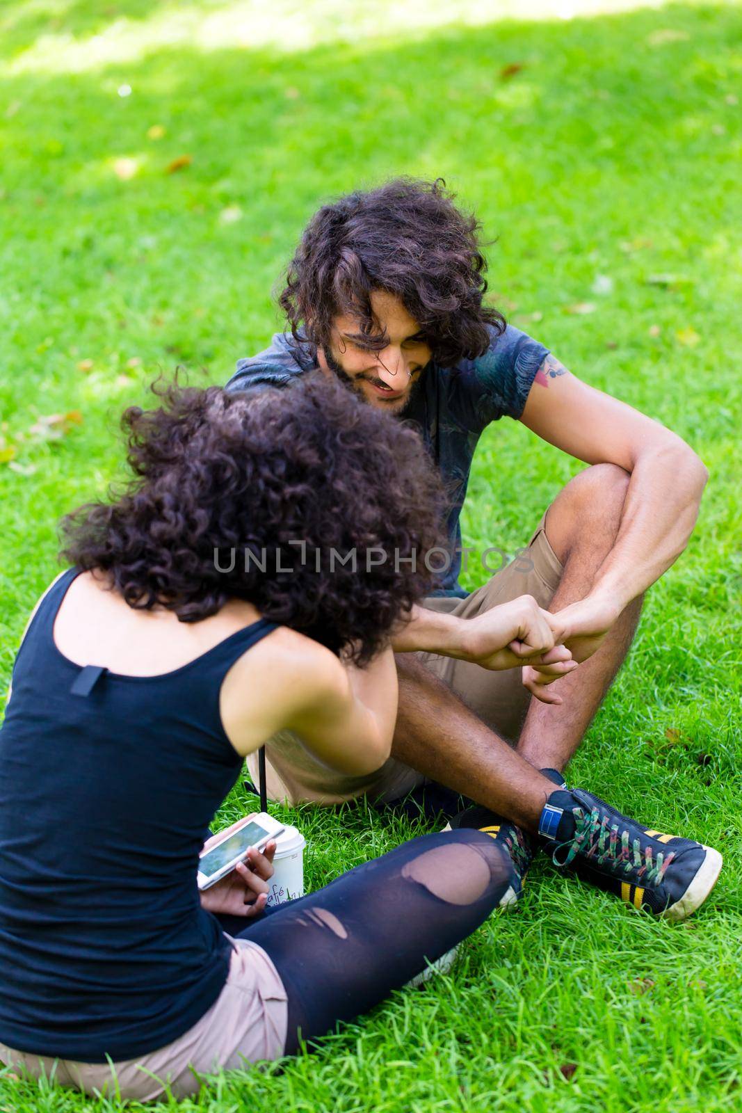 Latin Hipster couple sitting on meadow talking on summer day