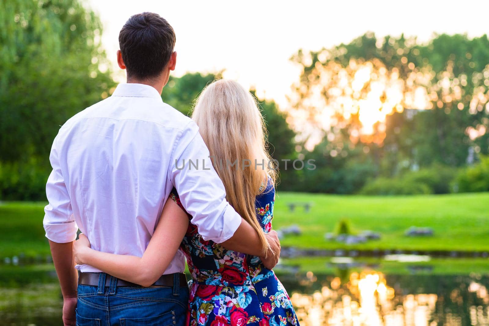 Couple dreaming their life together looking in romantic sunset, man embracing his girlfriend