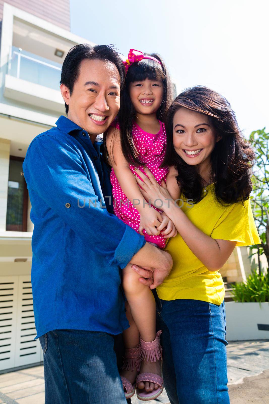 Asian Chinese family of parents and child standing proud in front of modern home