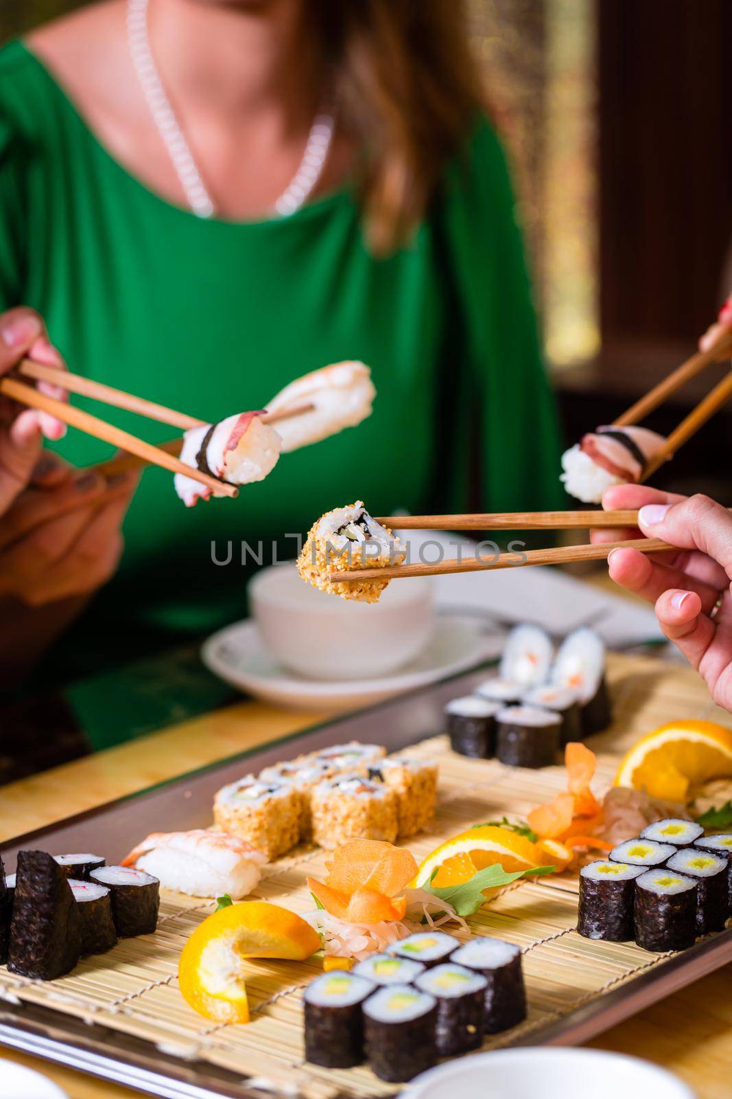 Young people eating sushi in Asian restaurant by Kzenon