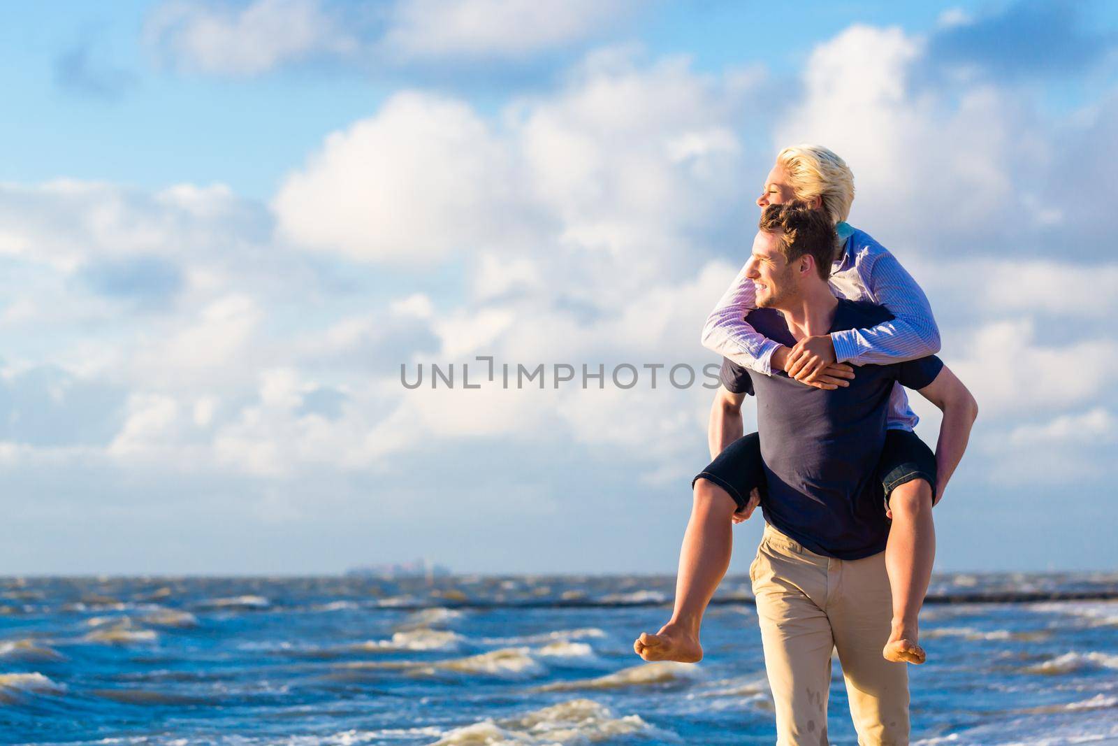 man carrying woman piggyback at beach by Kzenon