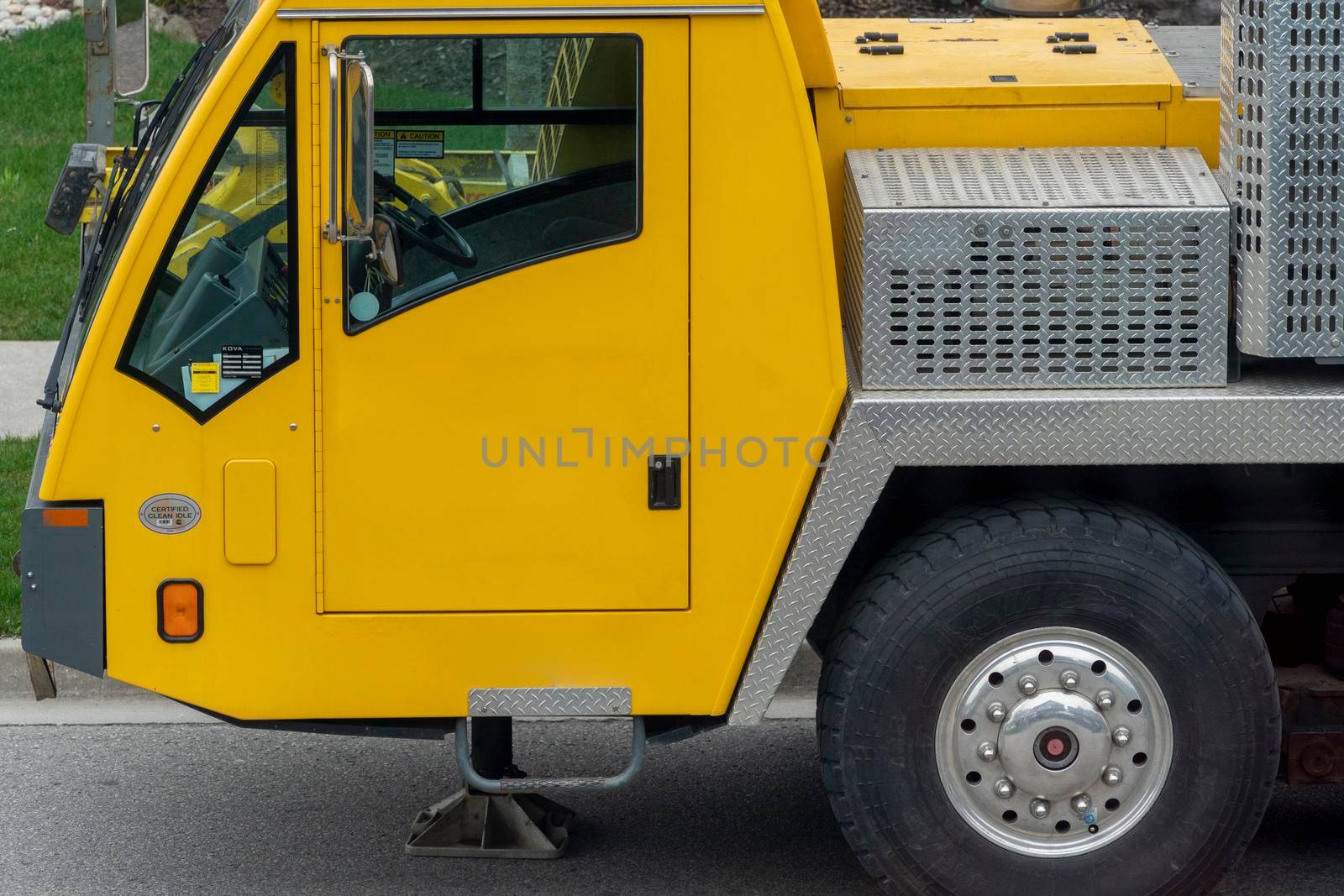 Fragment of a yellow truck crane cab, with a front wheel on the driver's side