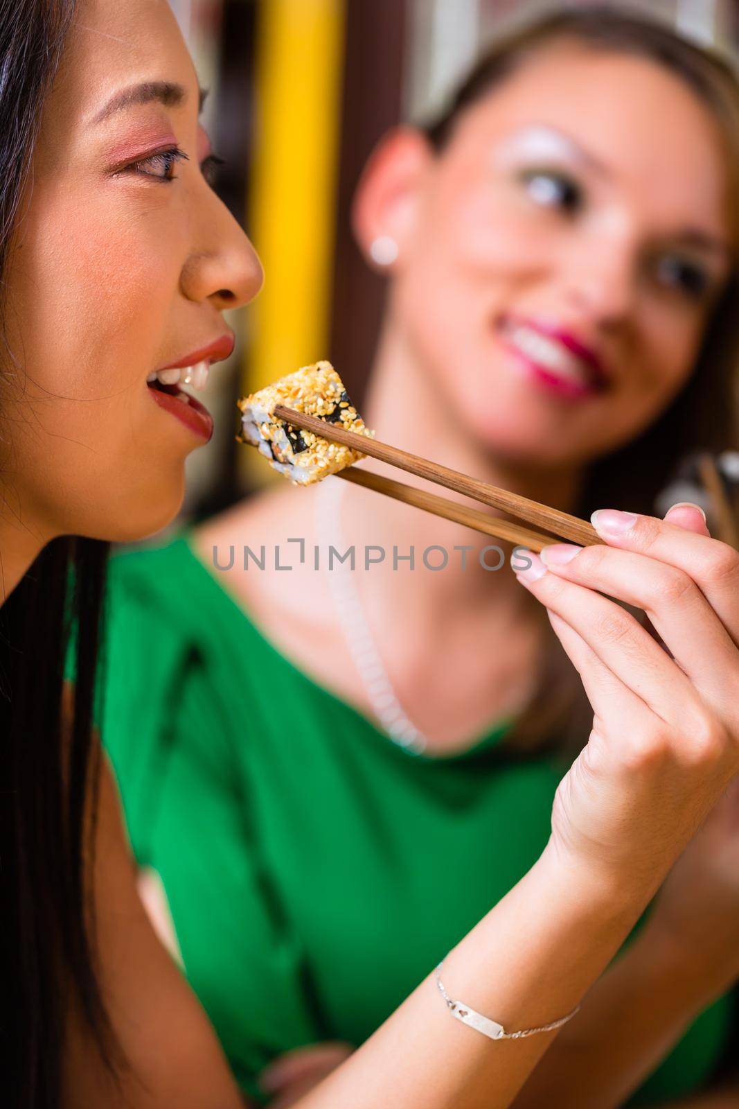 Young people eating sushi in Asian restaurant by Kzenon