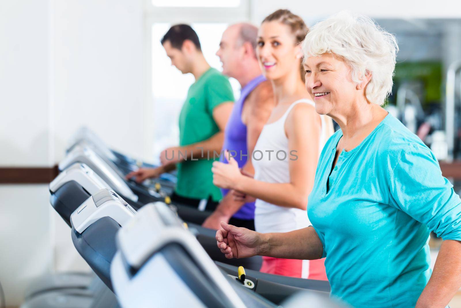 Group with senior and young men and women on treadmill in fitness gym running for sport