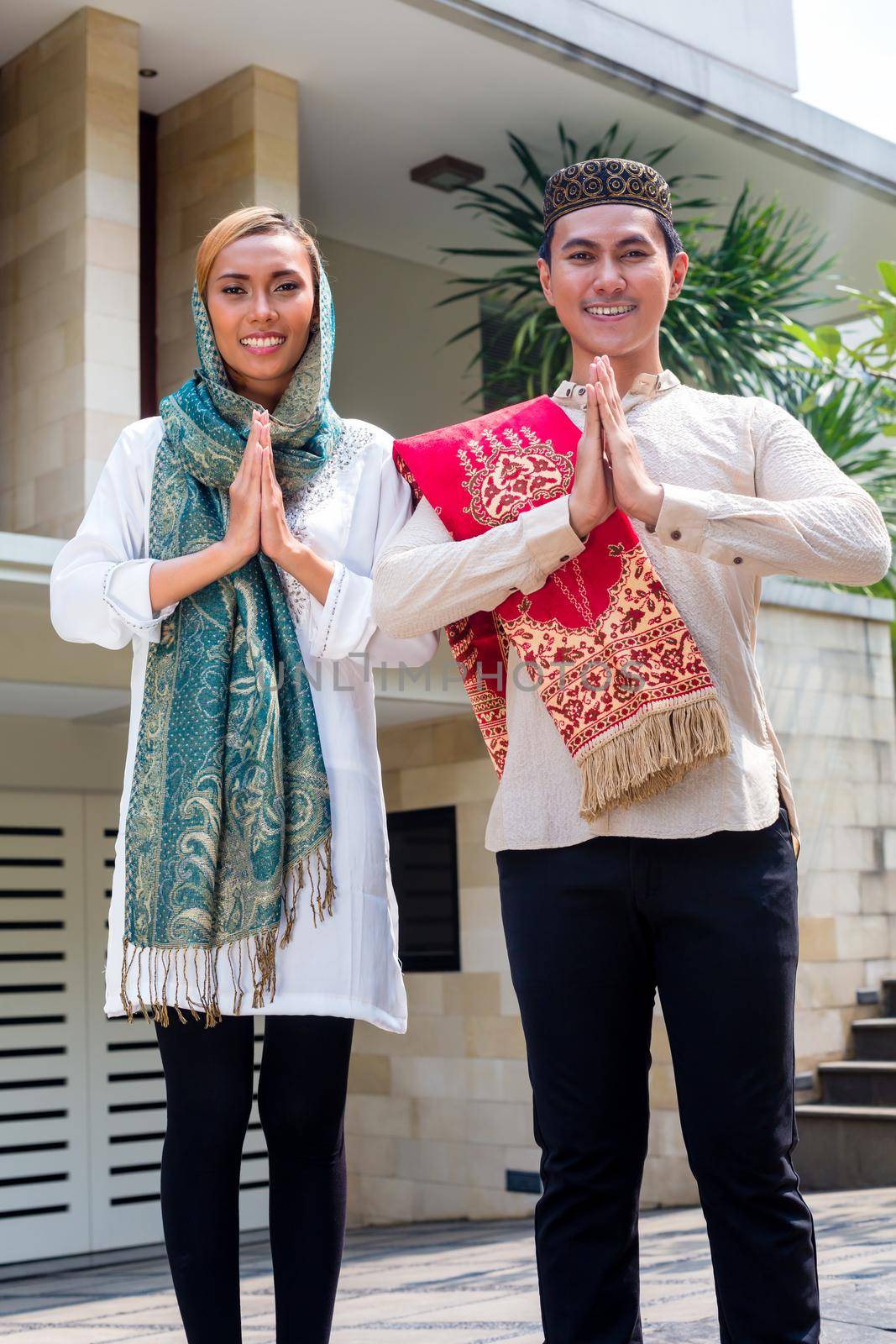 Asian Muslim man and woman welcoming guests wearing traditional dress