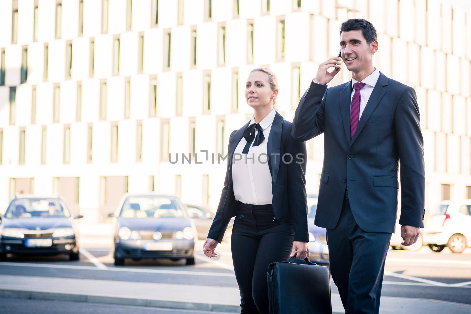 Business people in front of office building wearing briefcase and talking to smart phone