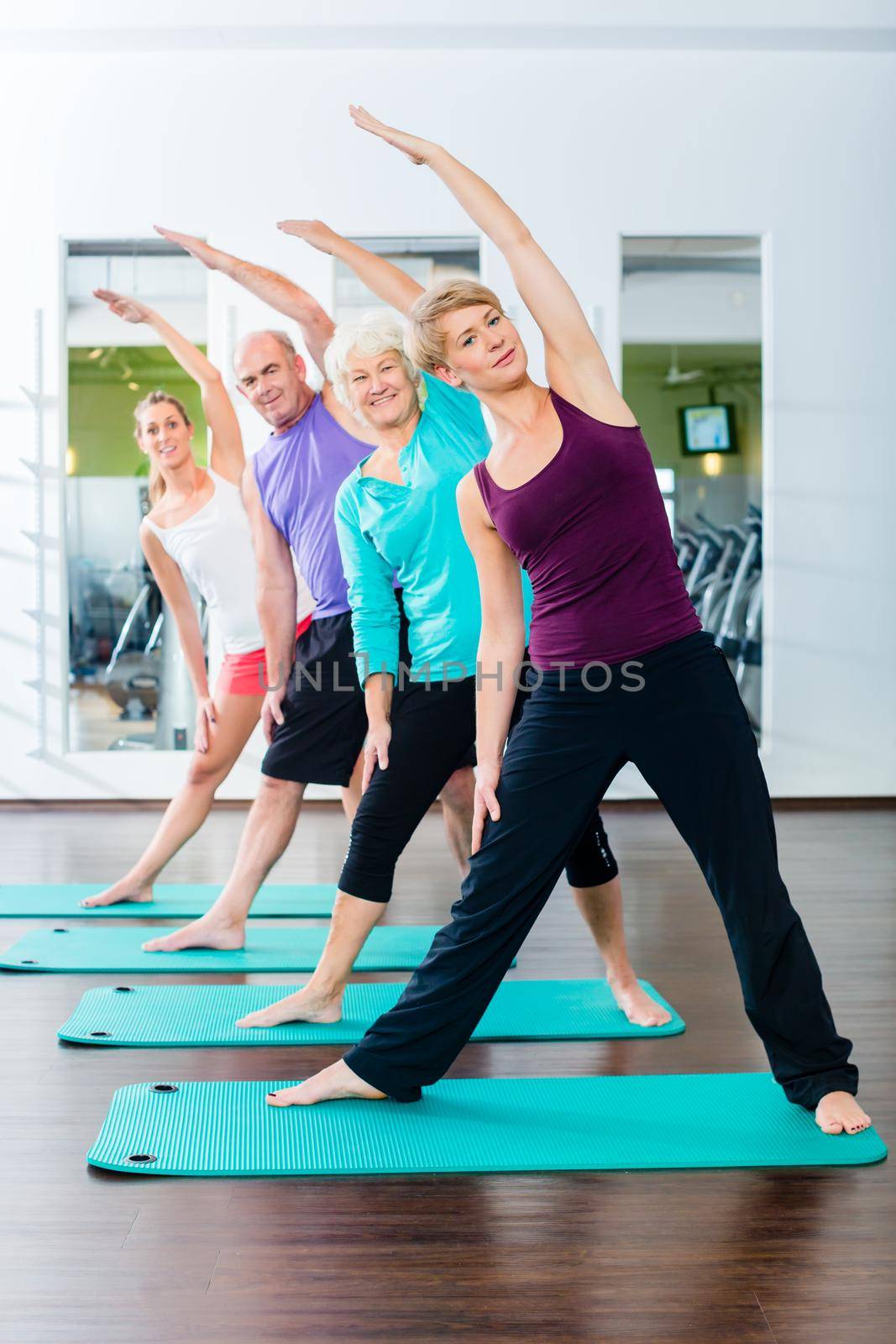 Group of senior people and young woman and men in fitness gym doing gymnastics