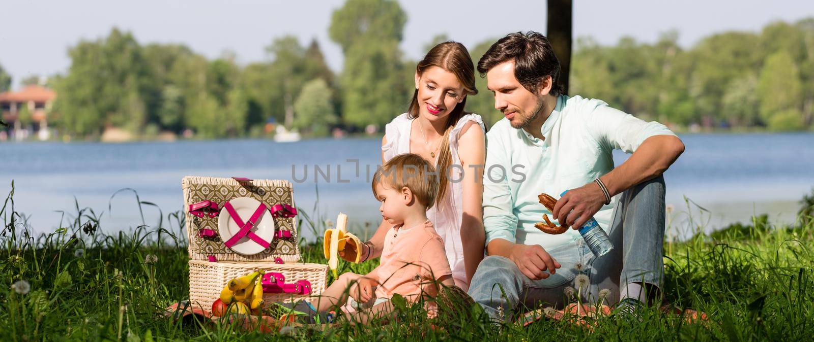 Family having picnic at lake sitting on meadow by Kzenon