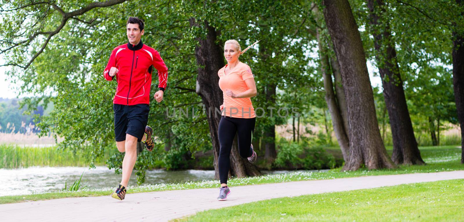 Woman and man jogging on dirt path in the woods together