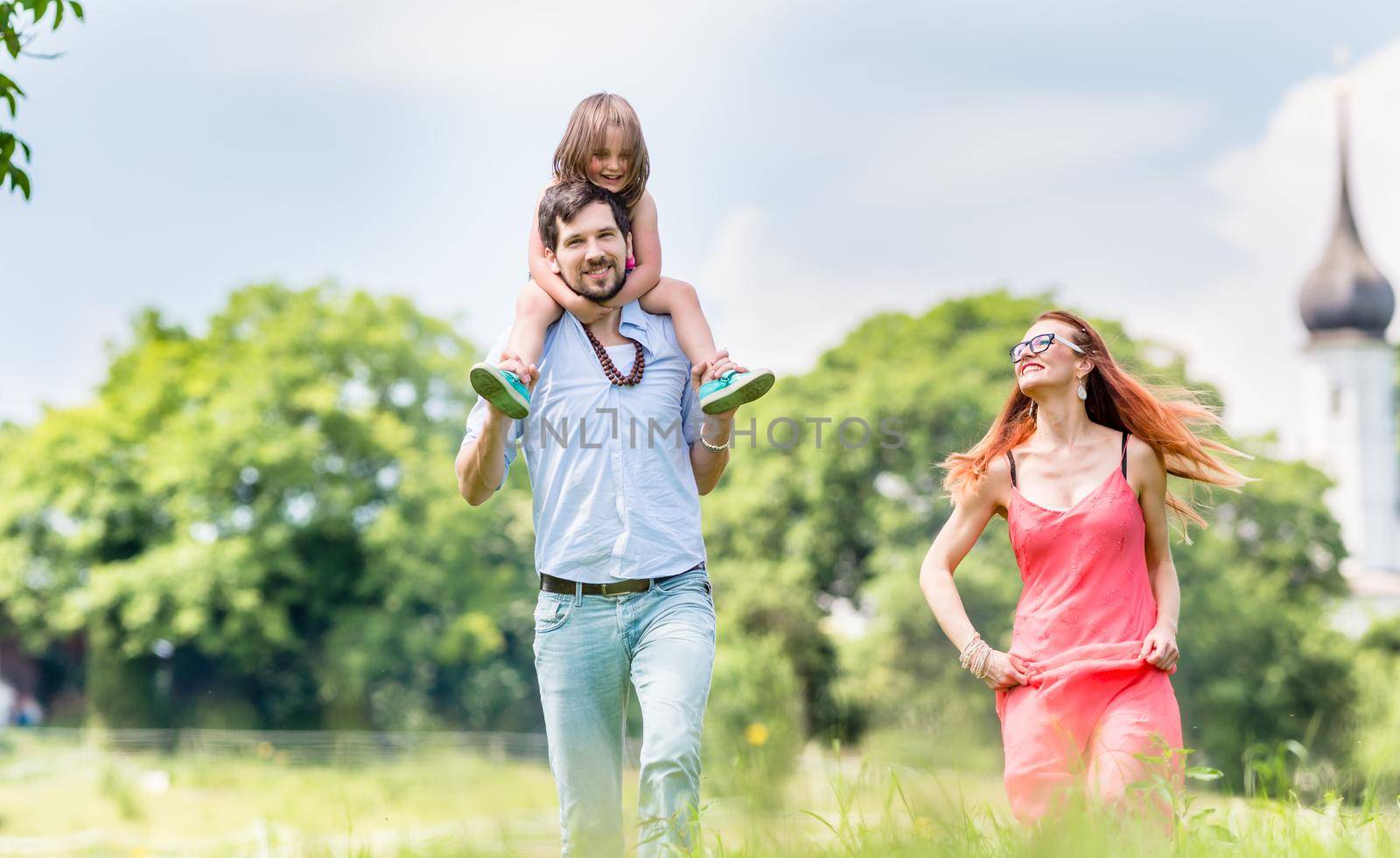 Family walking on meadow having walk, dad is carrying his little daughter on the shoulders