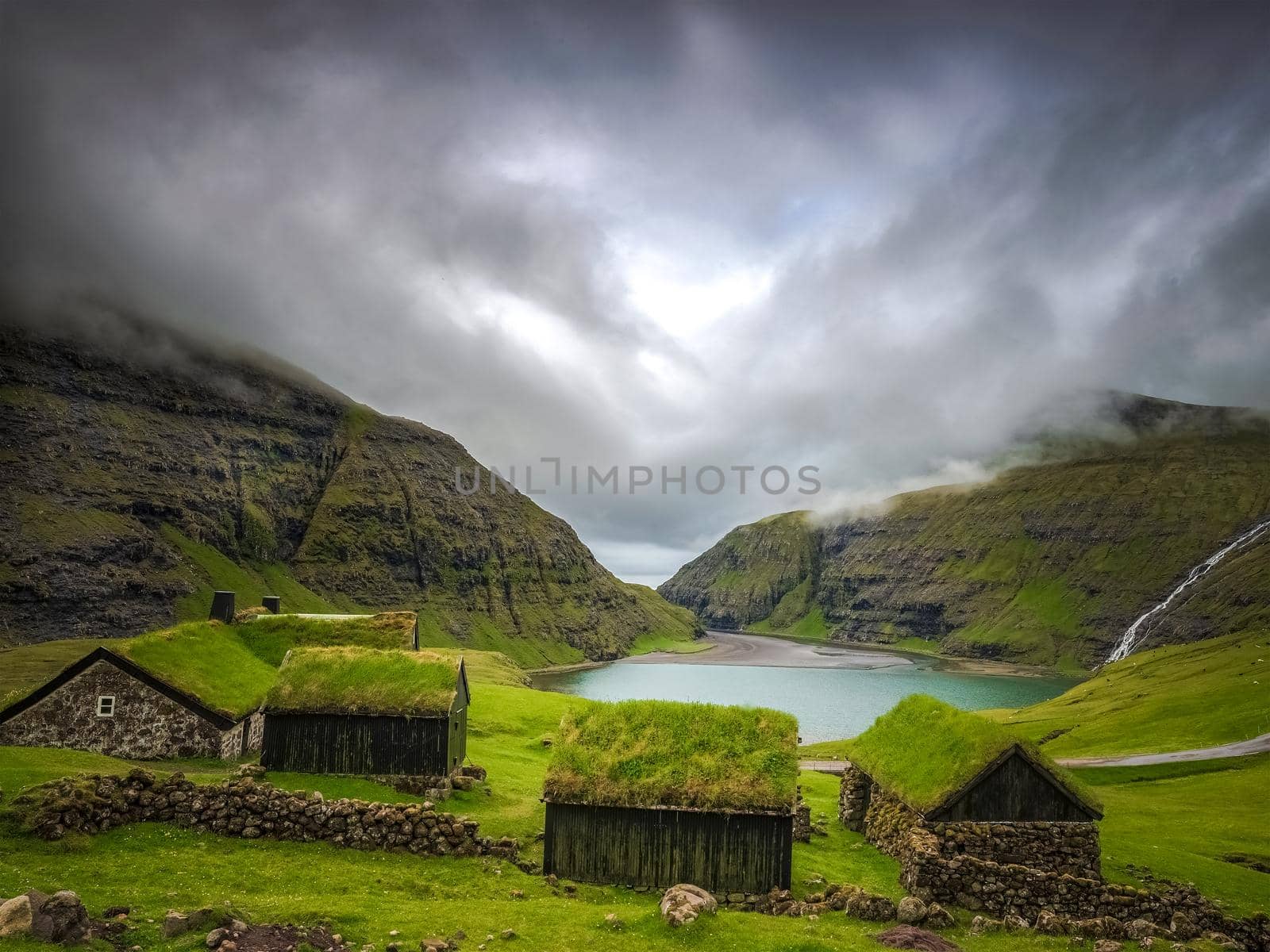 Small houses near a blue lake, a small house made of stones with covered grass on the shore of a beautiful lake by isaiphoto