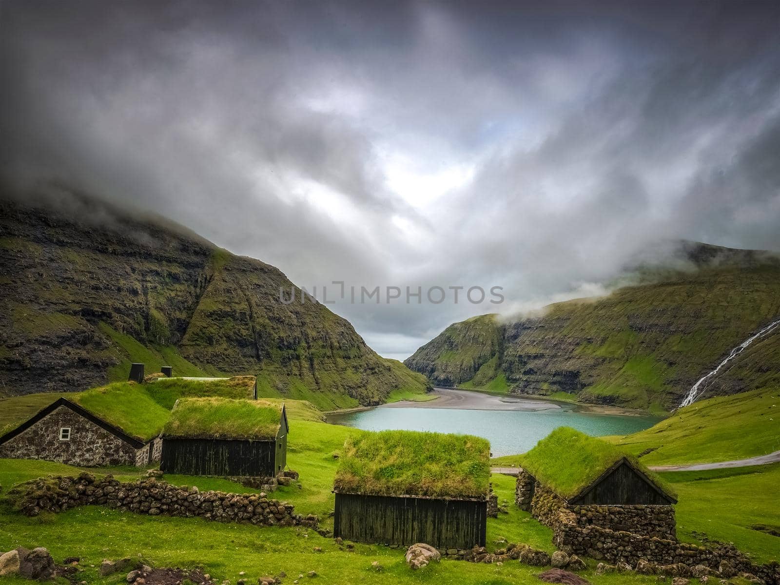 Small houses near a blue lake, a small house made of stones with covered grass on the shore of a beautiful lake