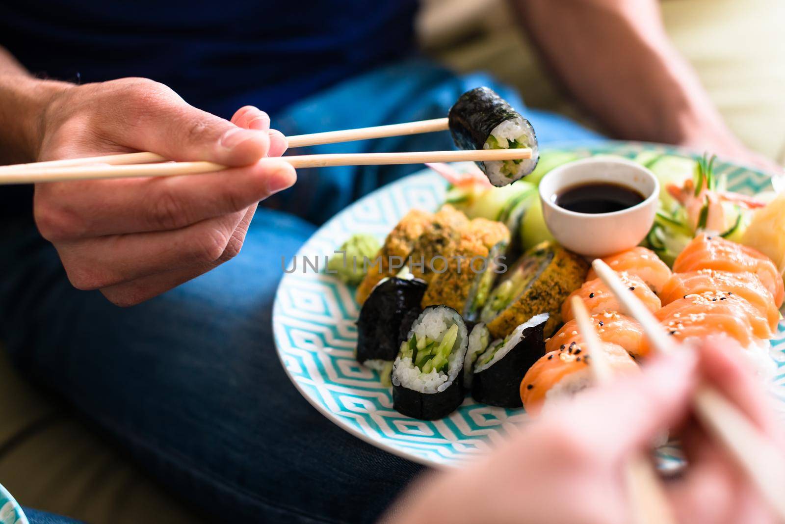 Close-up of the hands of a young couple eating traditional Japanese food with chopsticks during romantic dinner at home