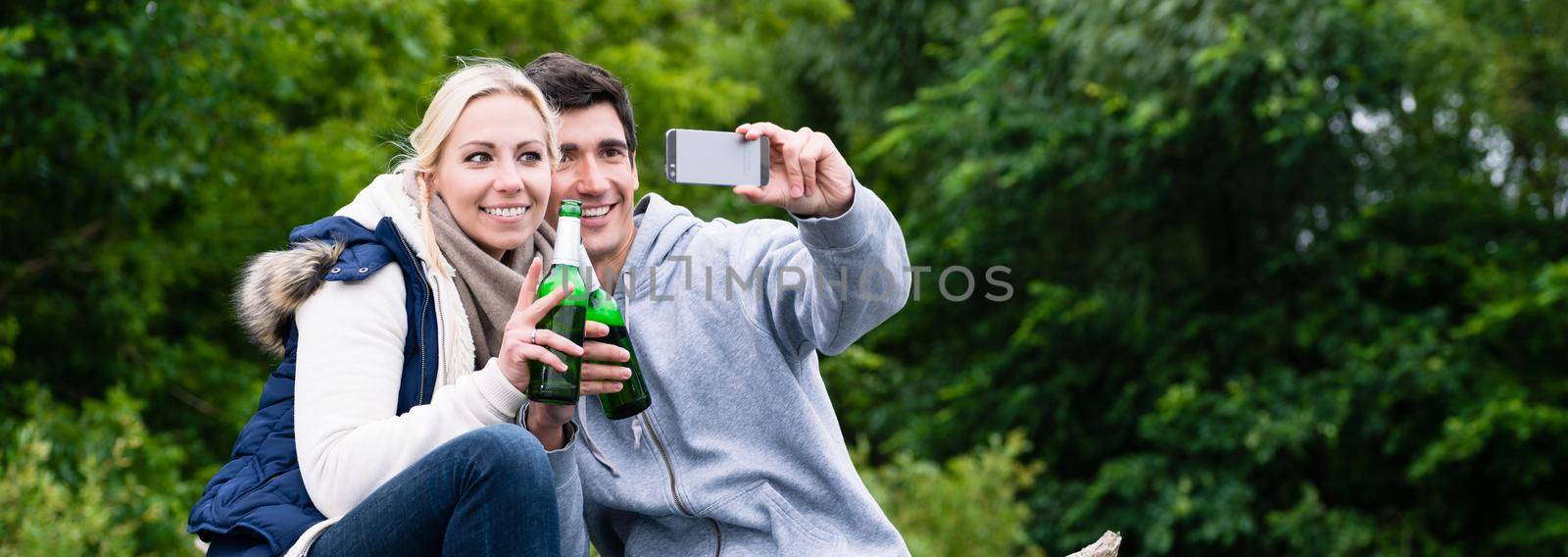 Woman and man drinking beer taking selfie while hiking in forest