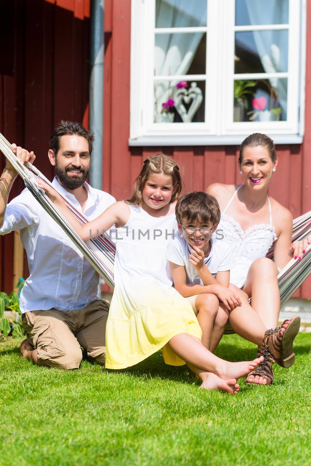 Family sitting in hammock in front of home by Kzenon