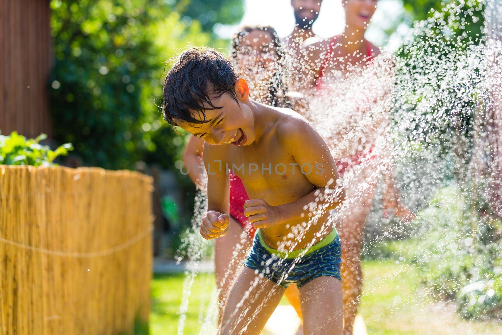 Family cooling down with sprinkler in garden by Kzenon