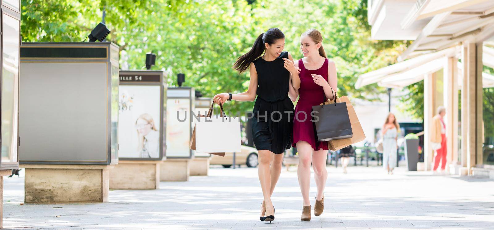 Two young beautiful women looking for fashion boutiques while carrying paper bags during shopping downtown in summer