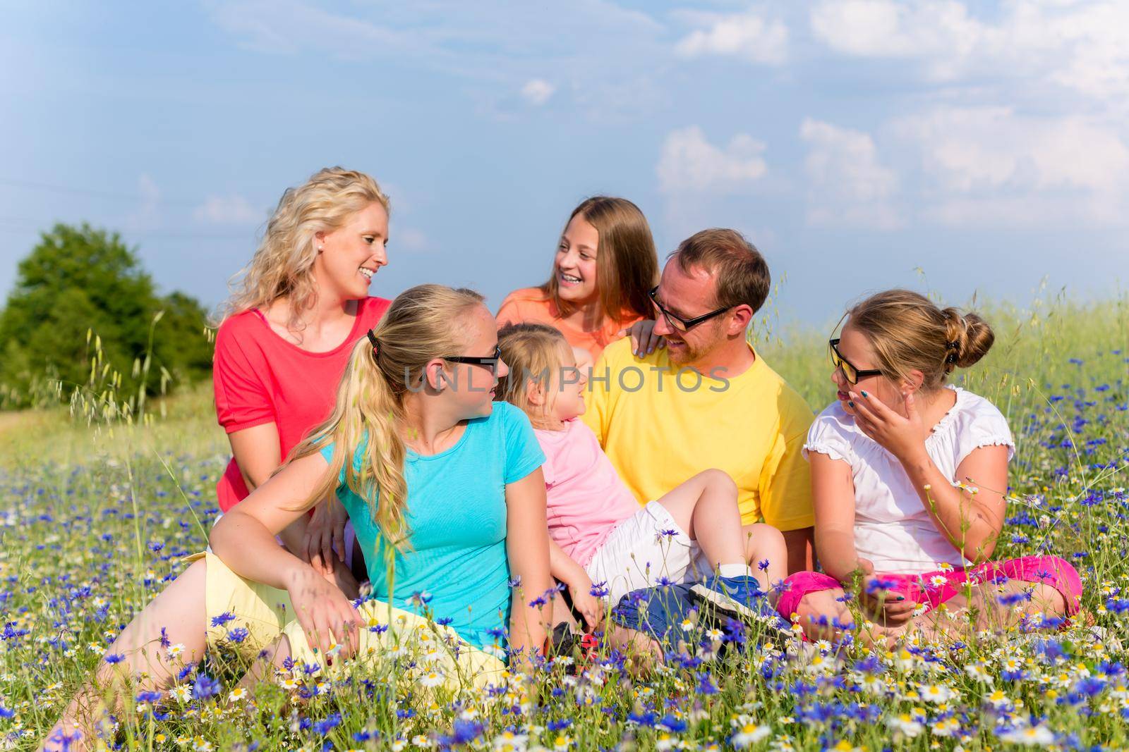 Family sitting on meadow in flowers by Kzenon