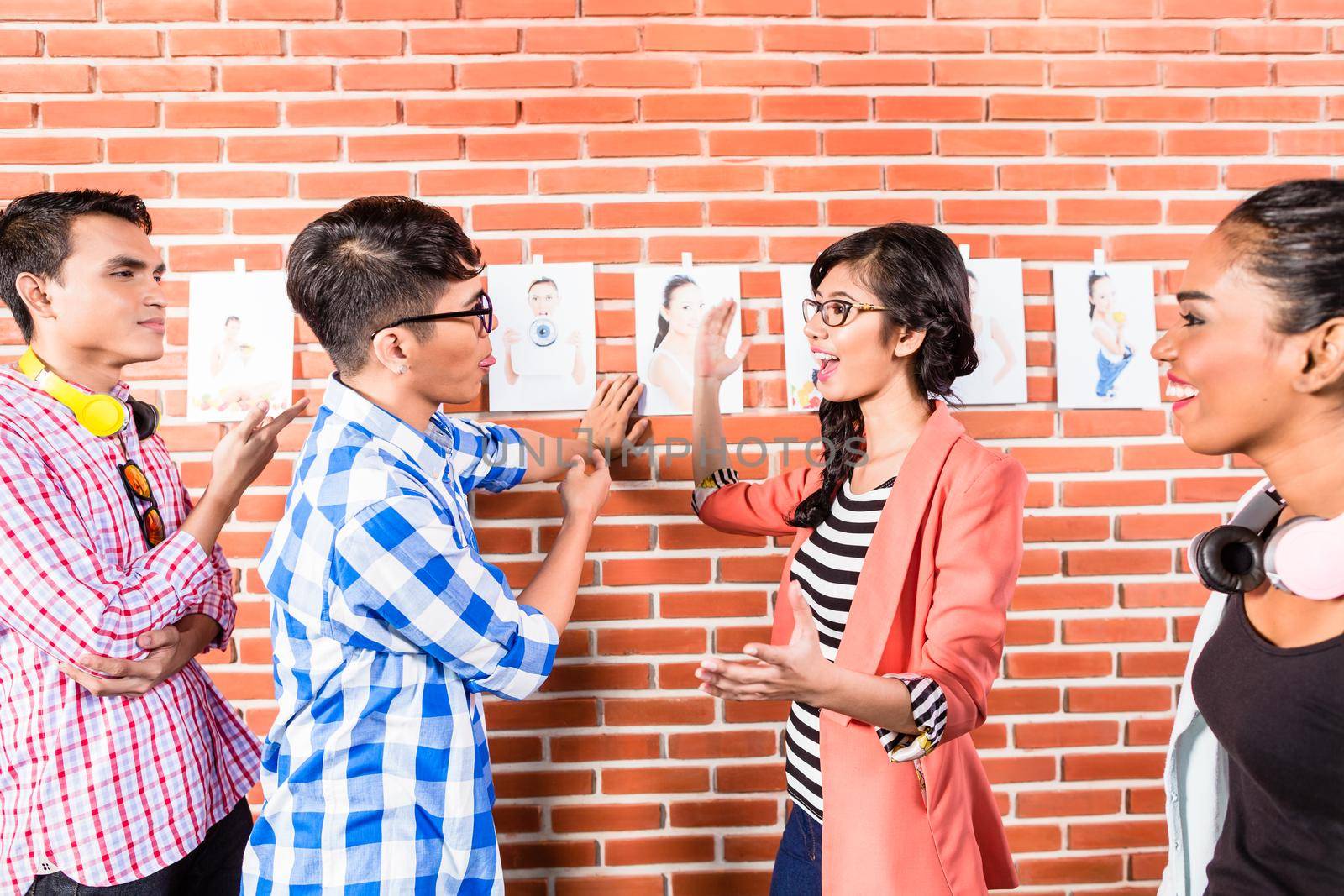 Advertising people choosing key visual among pictures of model hanging from wall