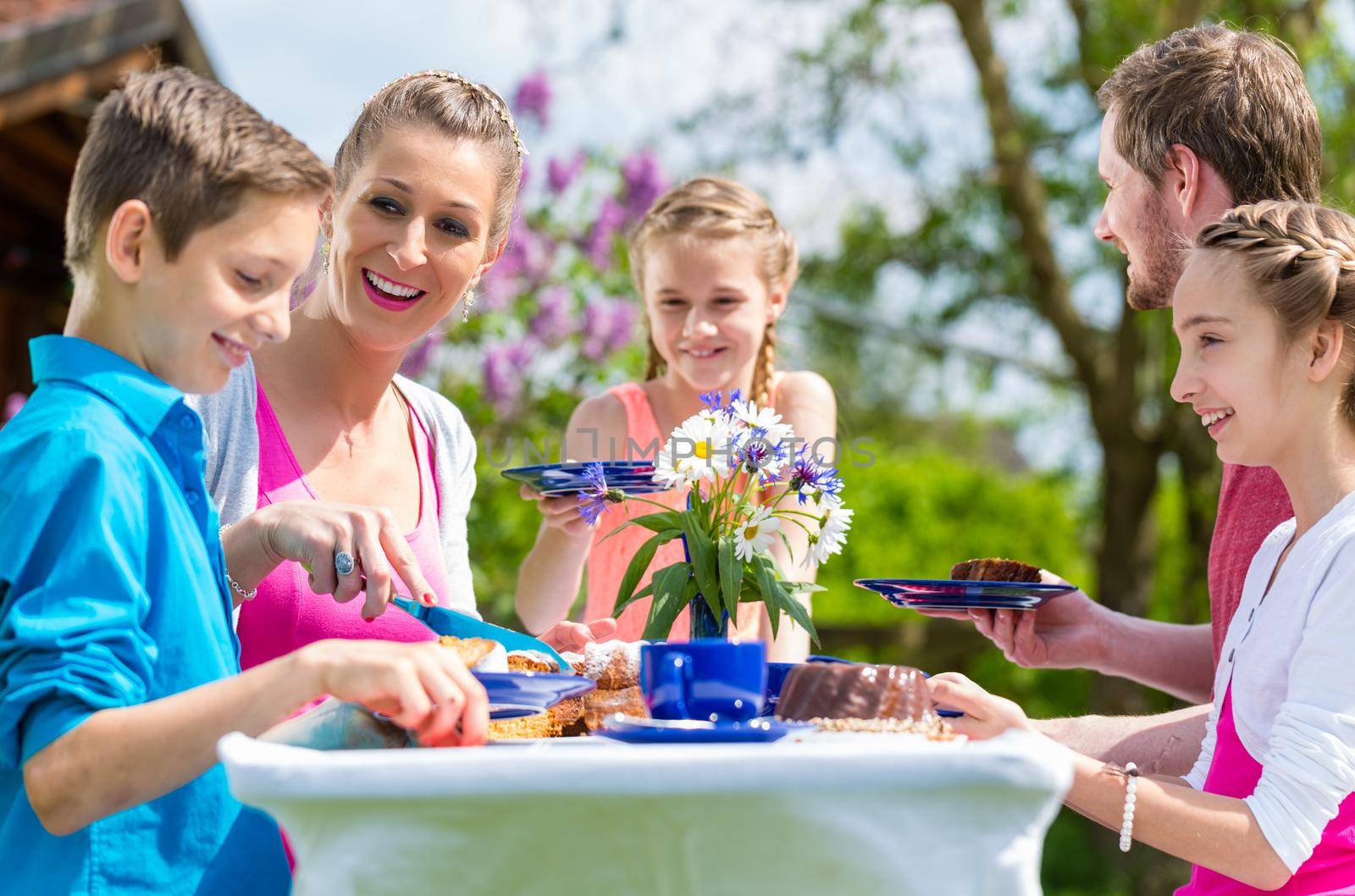 Family having coffee and cake in garden sitting in front of their home