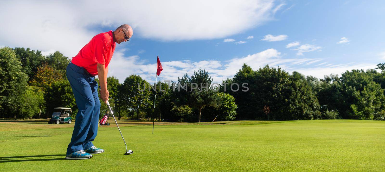 Senior golf playing man putting on green by Kzenon