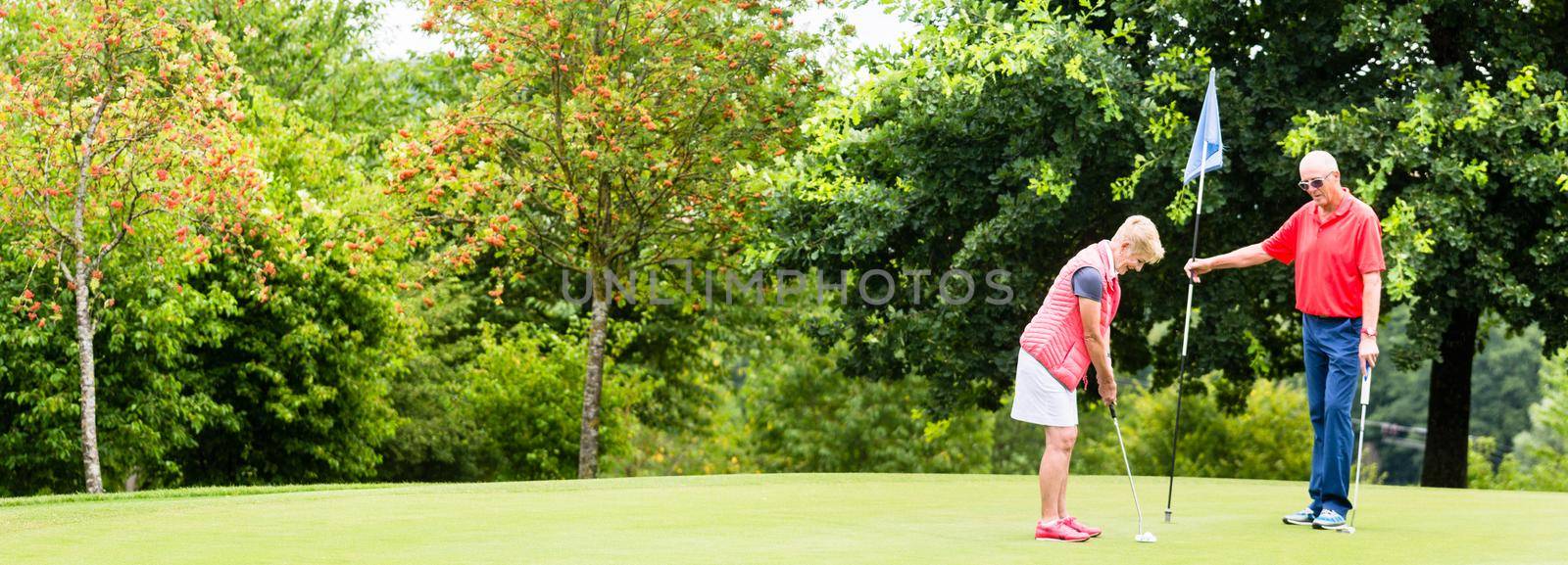 Senior woman and man playing golf putting on green by Kzenon