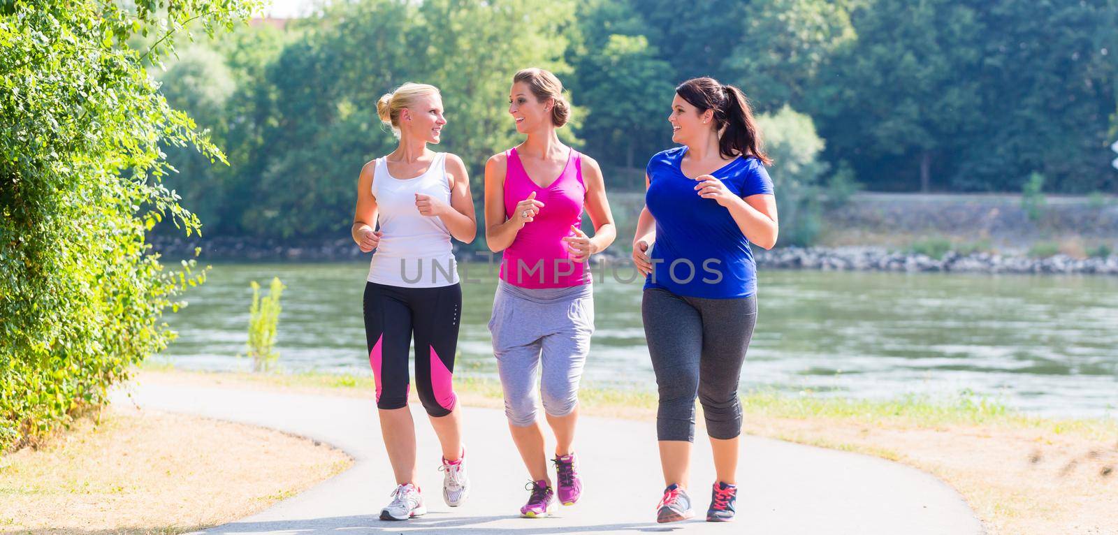 Group of women running at lakeside jogging by Kzenon