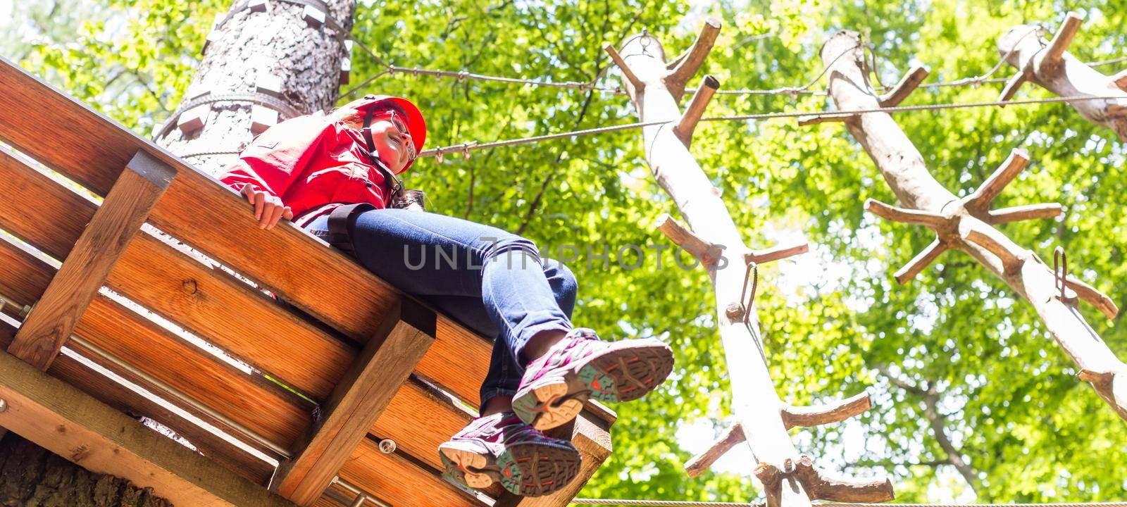 Girl sitting on platform in high rope course resting