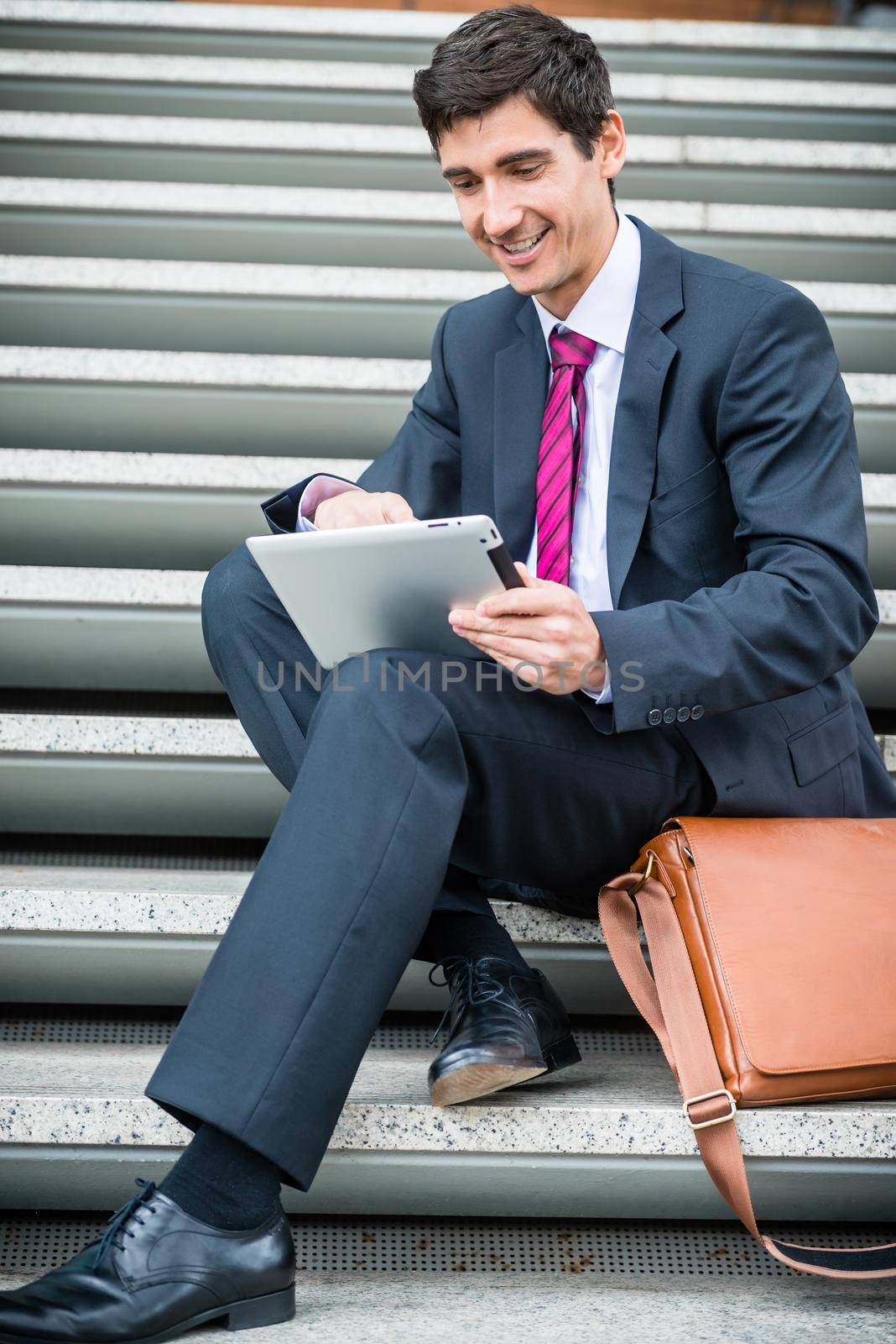 Young businessman smiling while using a tablet PC for online communication or data storage outdoors