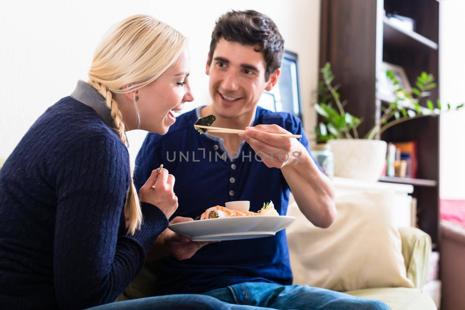 Funny young couple sharing Japanese traditional food during romantic dinner at home