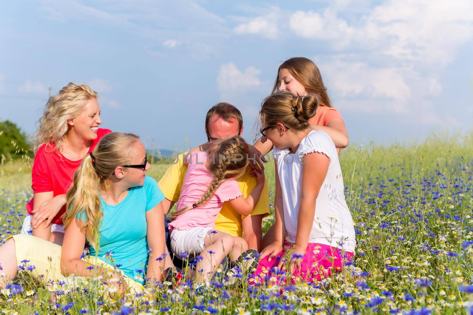 Family sitting on meadow in flowers by Kzenon