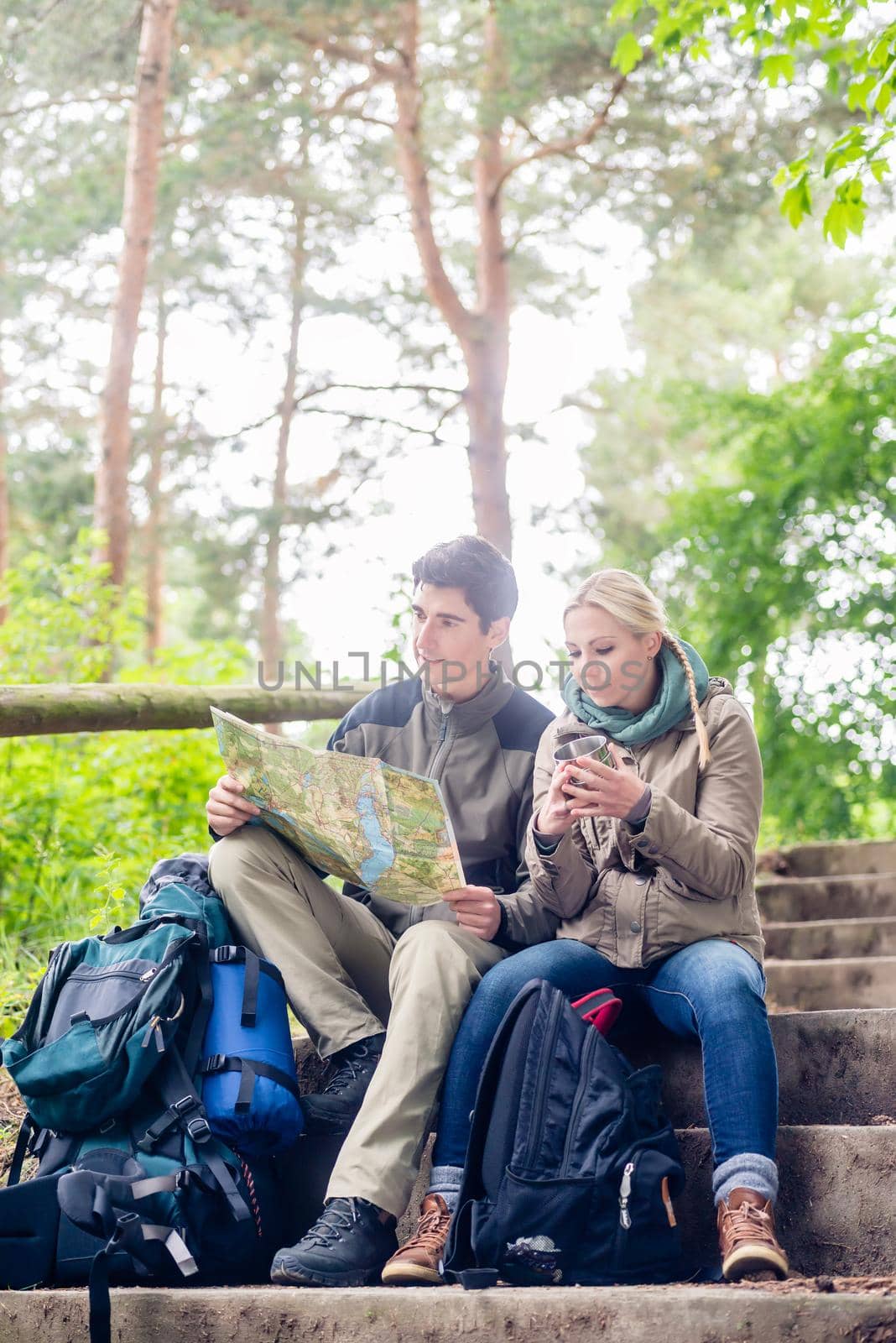 Hiking couple, woman and man, having break on a forest trail and reading the map