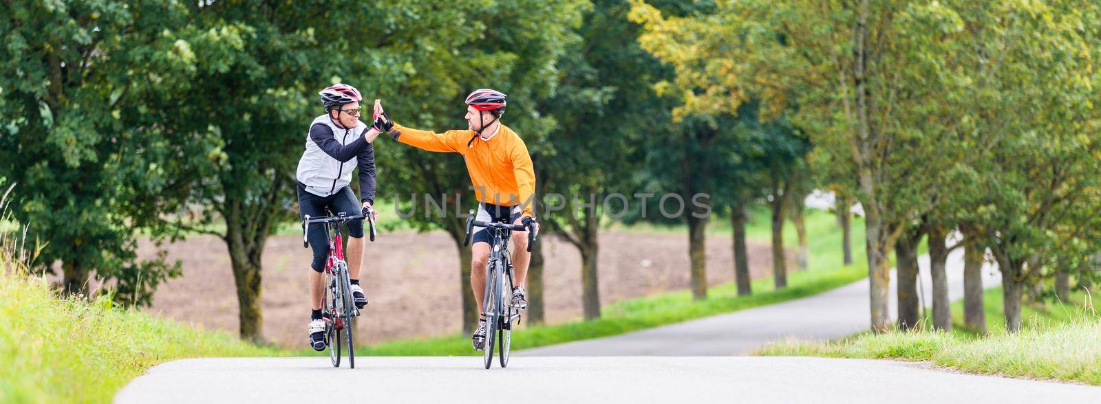 Racing cyclists after sport and fitness workout giving high five in finish