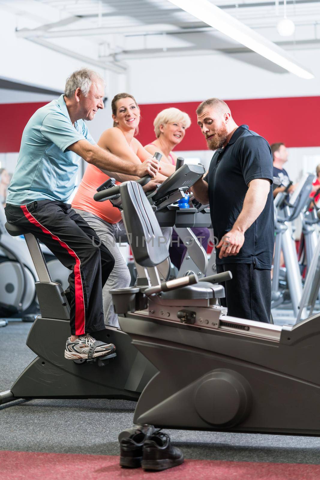 Group with senior man and woman spinning on fitness bikes with personal trainer at gym