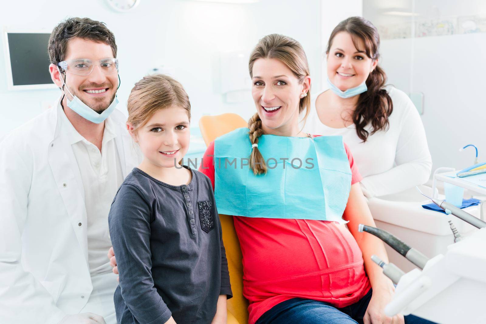 Dentist and his assistant with pregnant woman and child in surgery