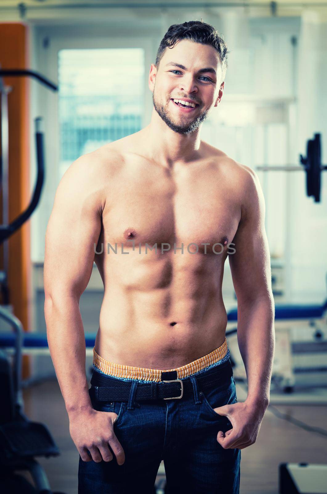 Trained athlete showing his muscles and six pack in health club gym