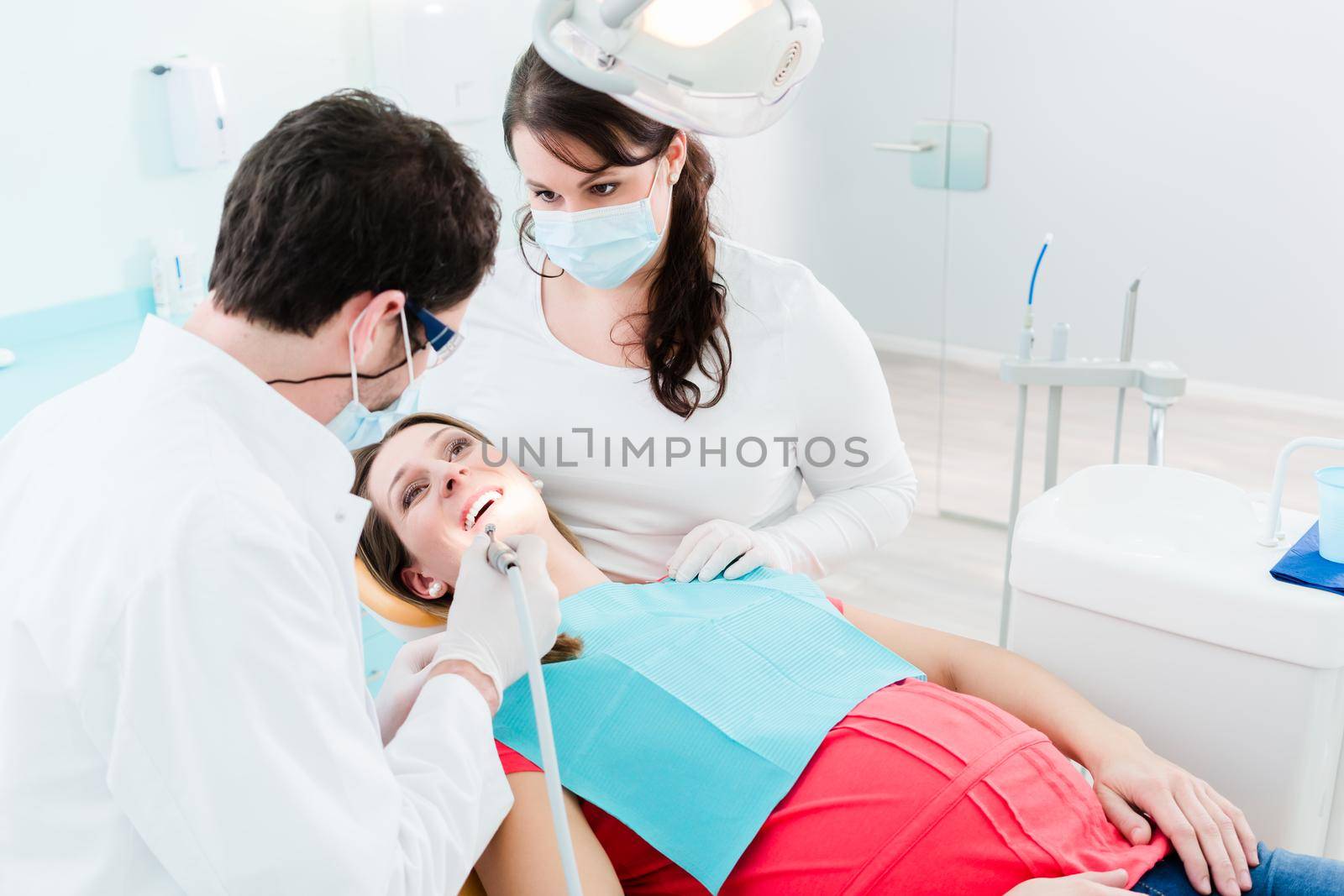 Dentist treating woman patient with drill by Kzenon